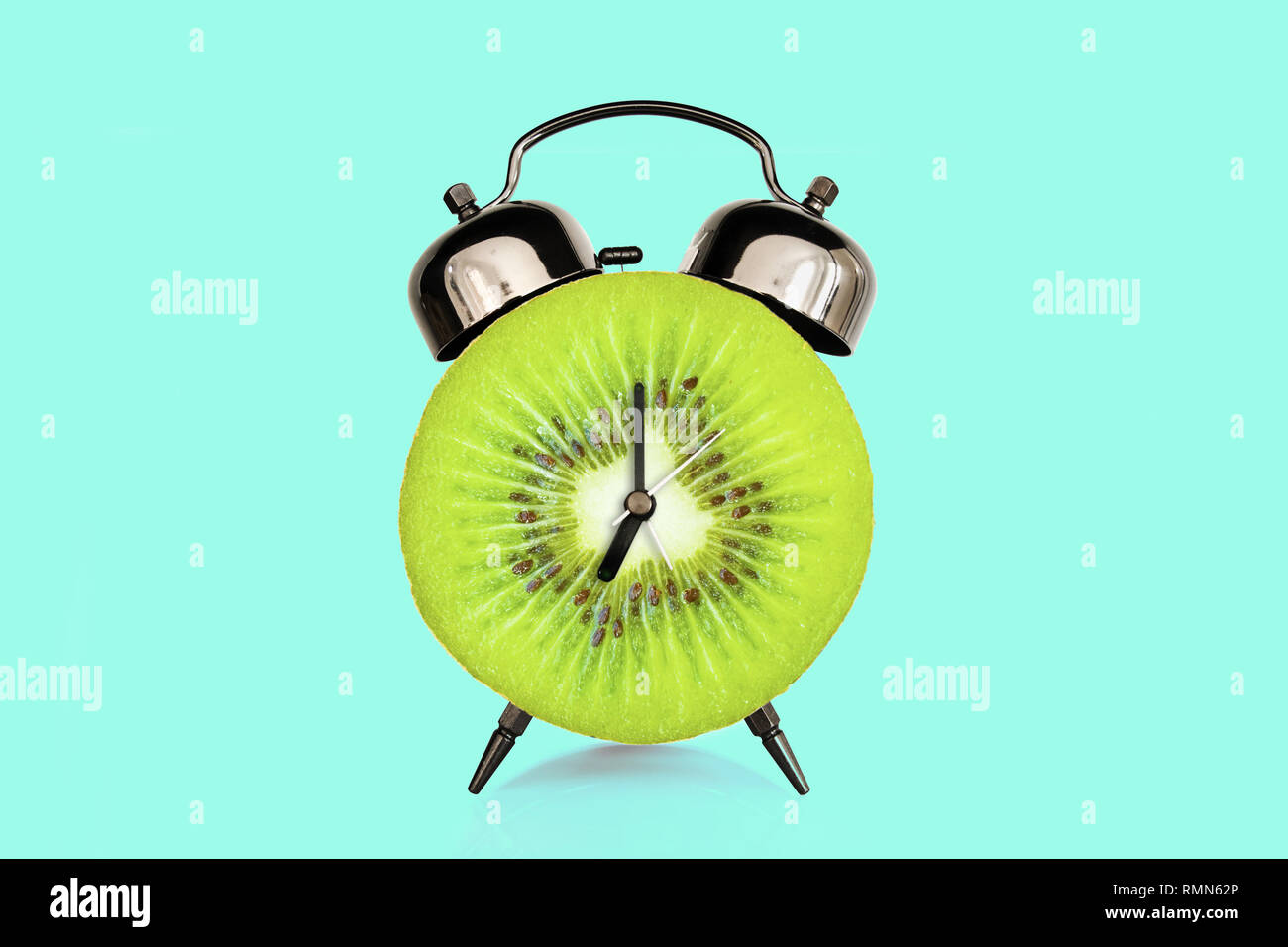 Rodaja de Kiwi reloj alarma, azul pastel. fondo de frutas y vitaminas dieta al concepto de nutrición desayuno Foto de stock