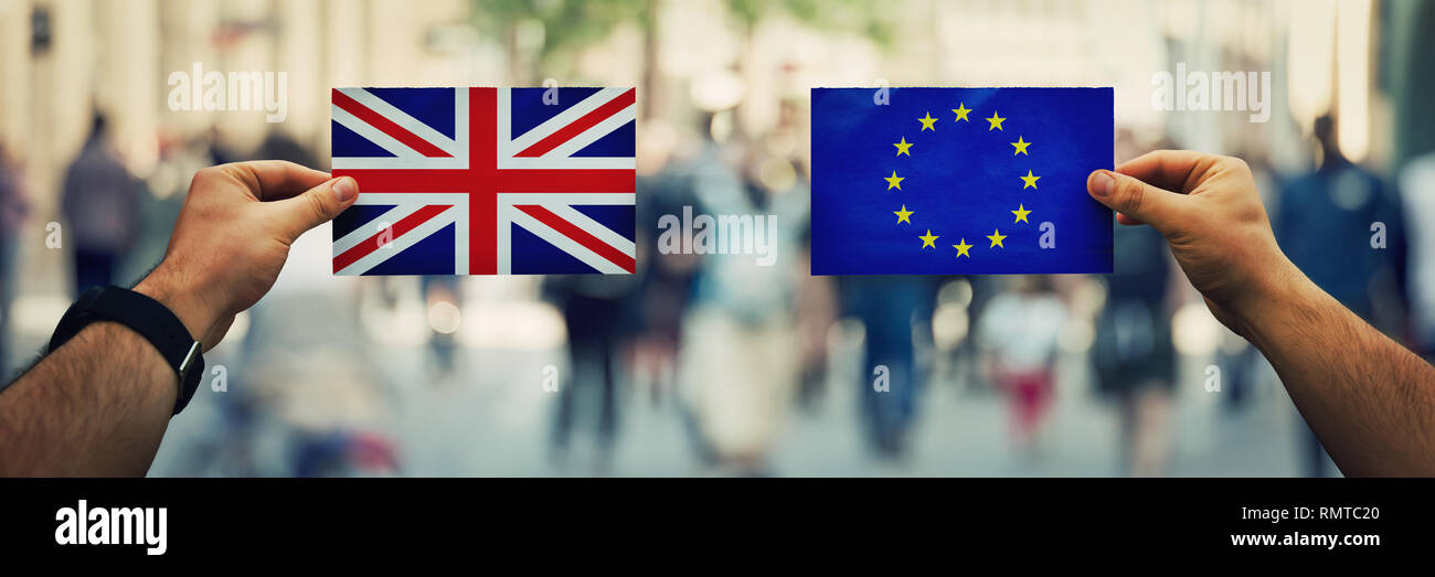 Dos manos sosteniendo diversas banderas, UE vs UK sobre política arena más concurrida calle de fondo. La estrategia futura de las relaciones entre los países después de brexi Foto de stock