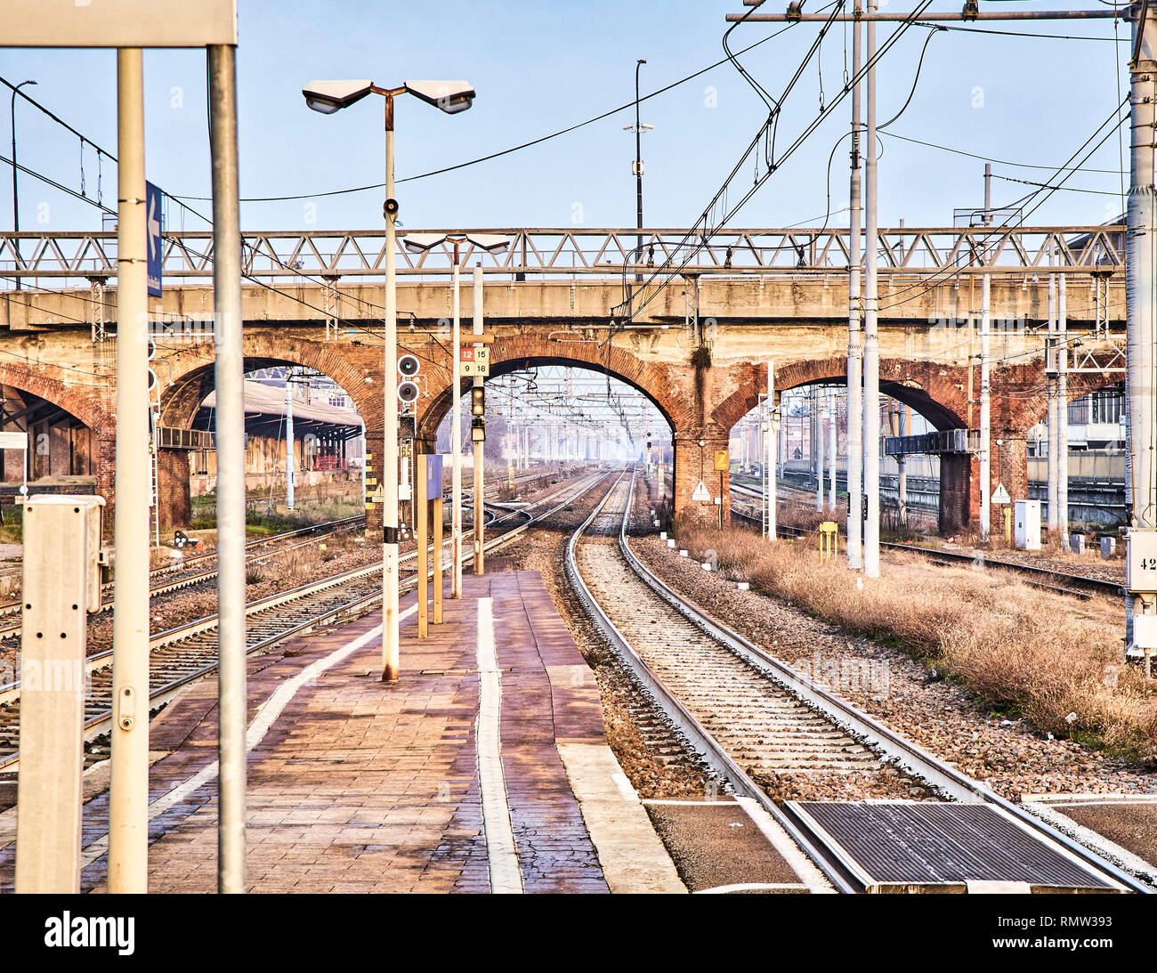 Ferrocarril con catenarias cruzando un viejo puente de ladrillos en una estación de tren europeo. Foto de stock