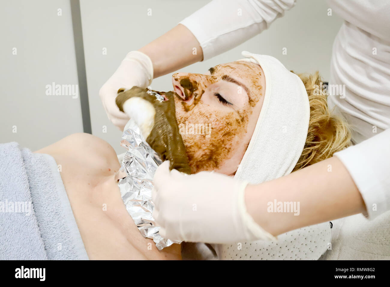 Trabajador esteticista eliminar descriptivos de mar algae mascarilla facial para la lucha contra el envejecimiento y la hidratación de la piel del cliente femenino en el salón de belleza cerrar Foto de stock