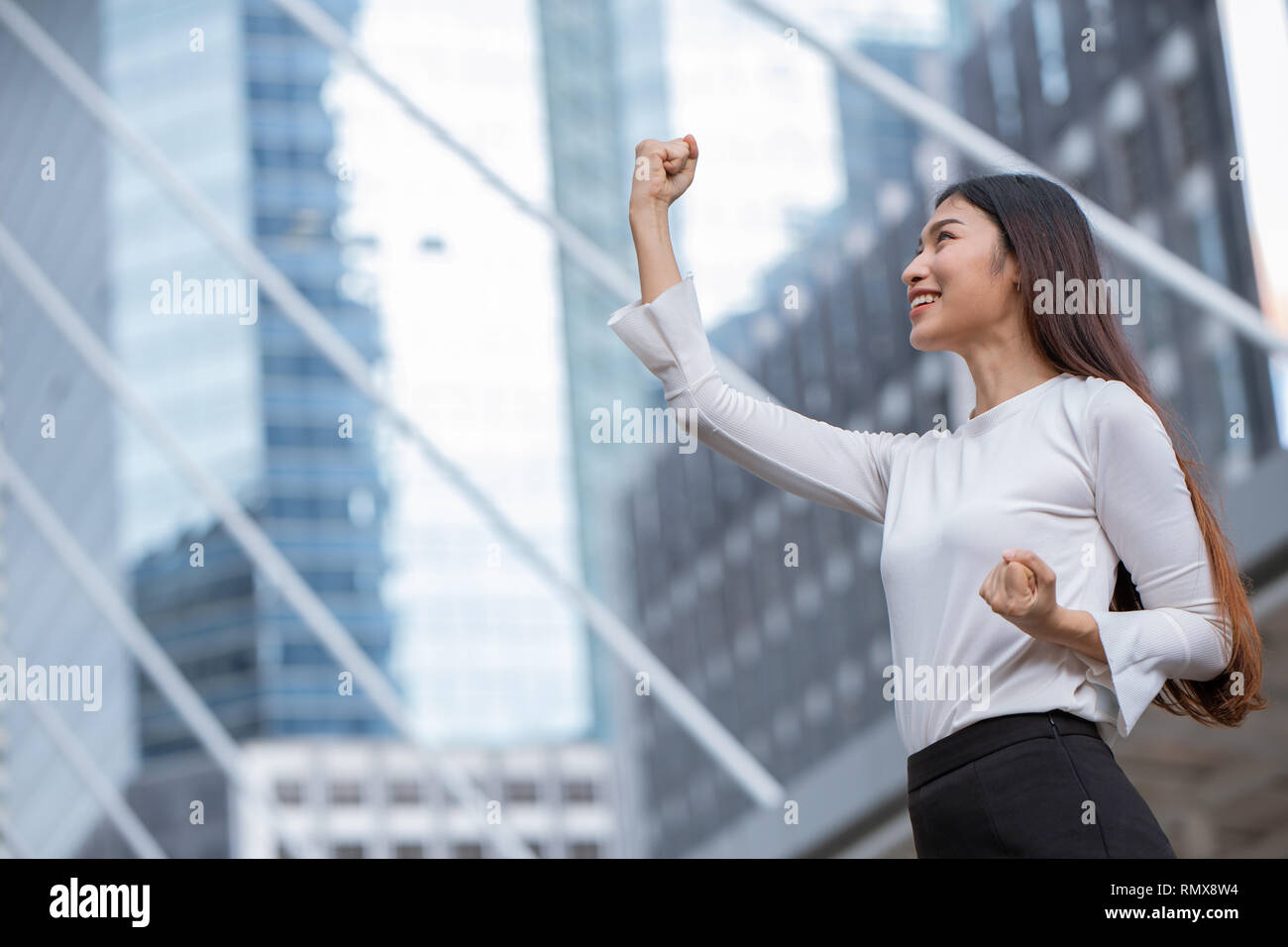 Las mujeres aumentan su mano para negocios ganador éxito concepto con el edificio de oficinas de fondo. Foto de stock