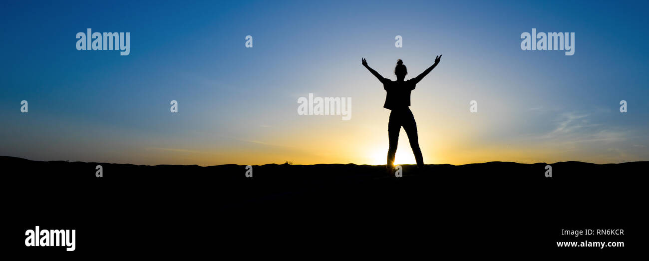 Silueta de una mujer de pie con los brazos en alto, en la puesta de sol Foto de stock