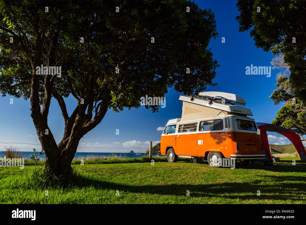 Jackson Bay, Coromandel, Nueva Zelandia, rojo VW Bully es acampar en la orilla de la playa, rodeado de árboles Foto de stock