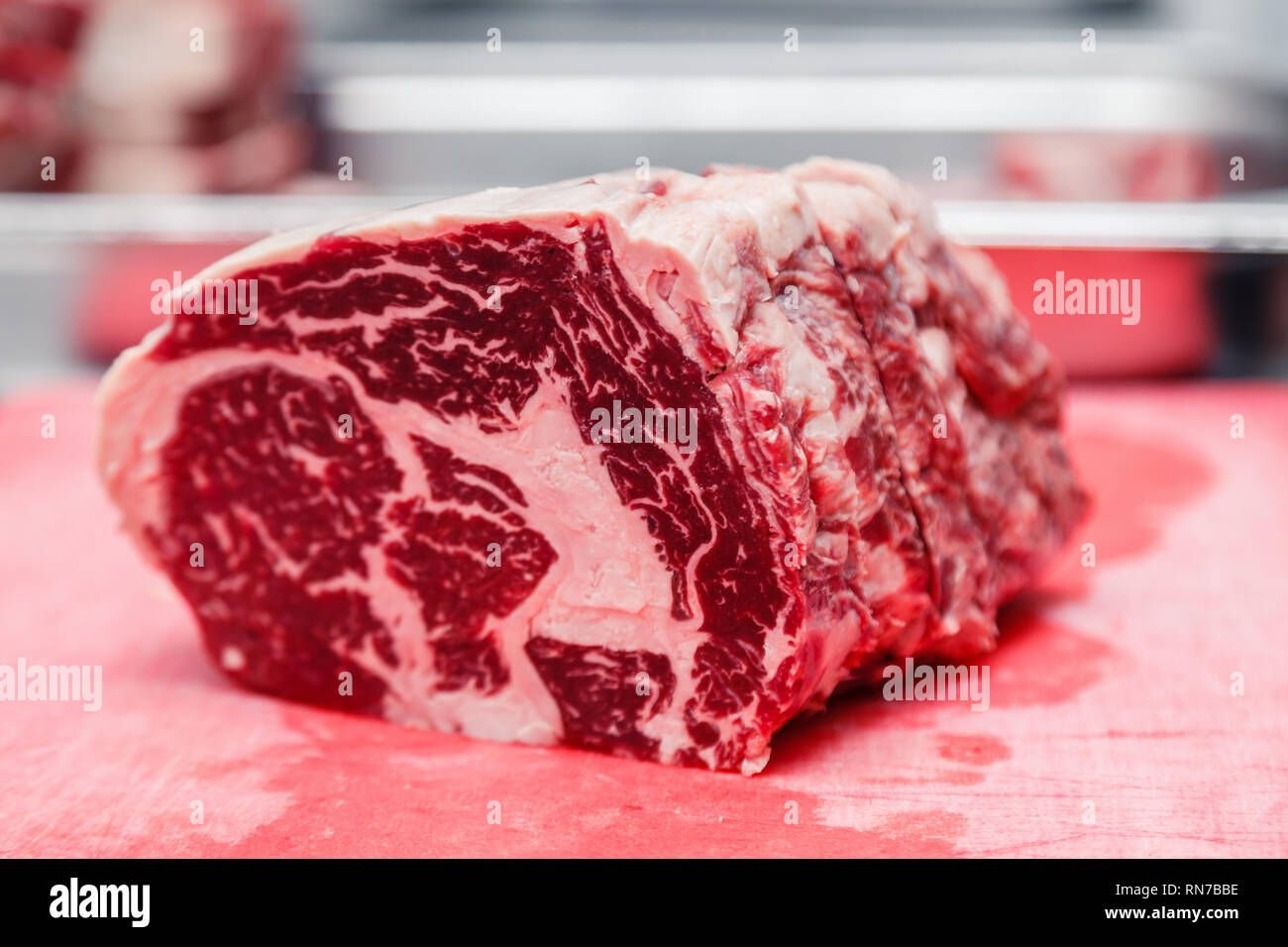 Closeup macro piezas chuletón de carne de mármol steak en la tabla de cortar de plástico rojo sobre la mesa metálica en el restaurante de cocina. Concepto de embalaje producción semi-acabados Foto de stock