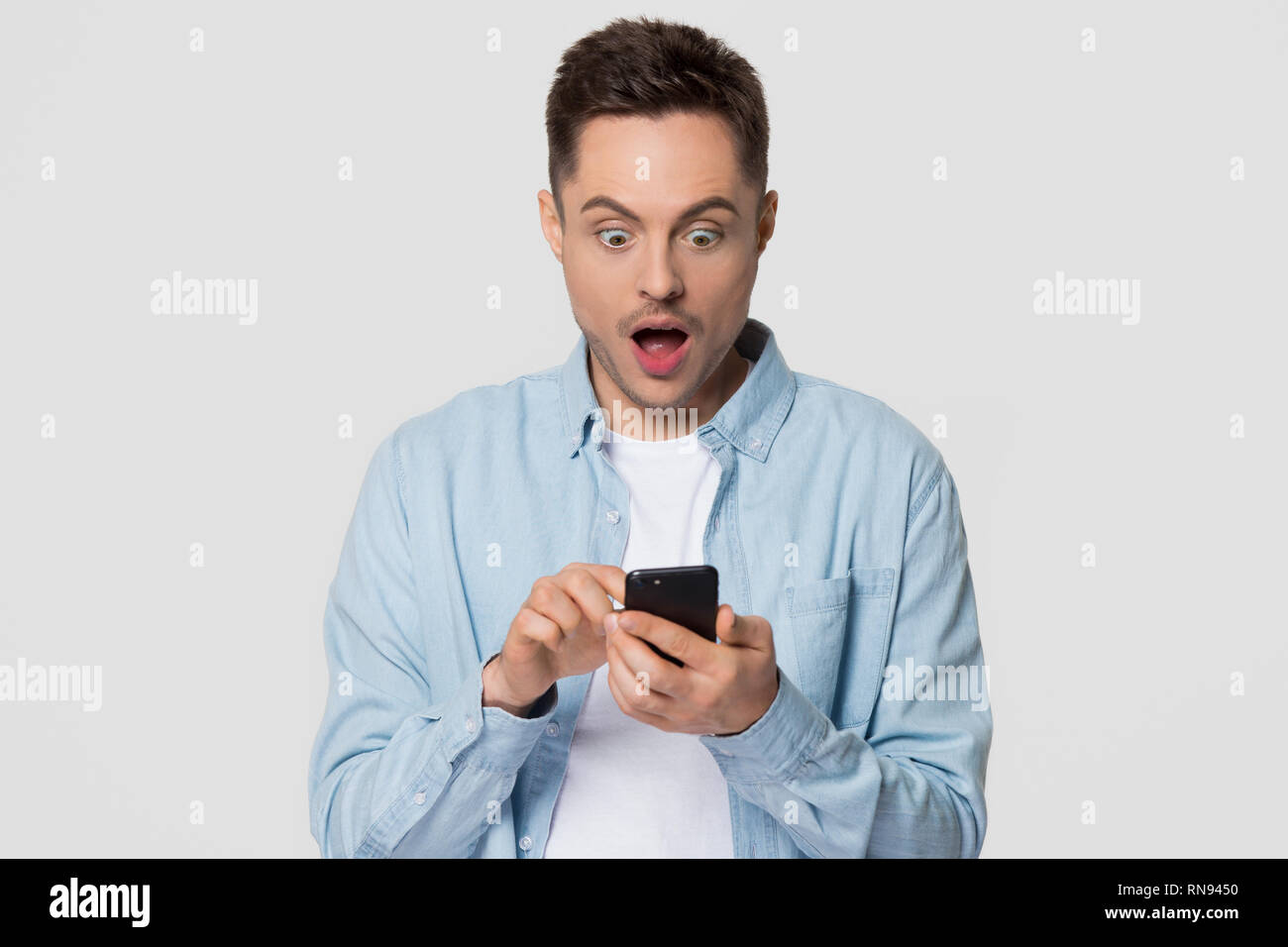 Sorprendido guy holding móvil mirando asombrados por teléfono noticias Foto de stock
