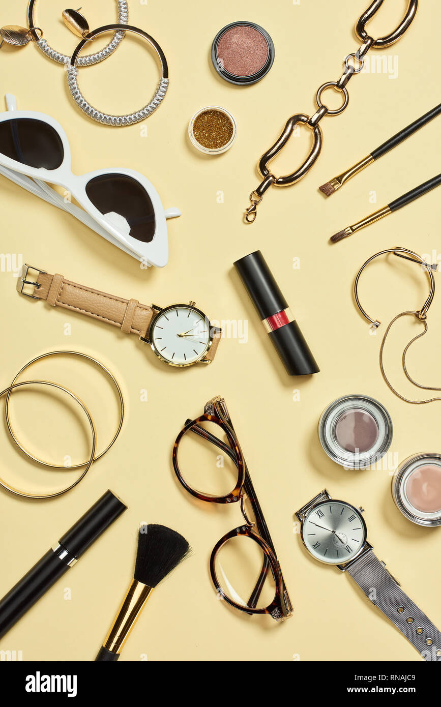 Vista superior de los relojes, lápiz labial, gafas, lentes de sol, sombreador de ojos, rubor, cepillos cosméticos, pulseras, aretes y rimel Foto de stock