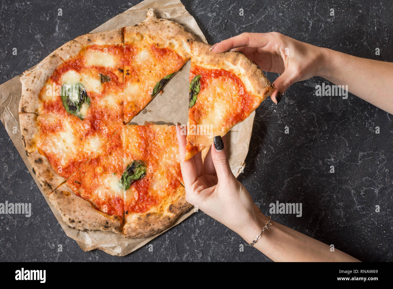 Mantenga las manos femeninas porción de Pizza Margherita en black mesa de piedra. Comida italiana tradicional. Vista superior Foto de stock