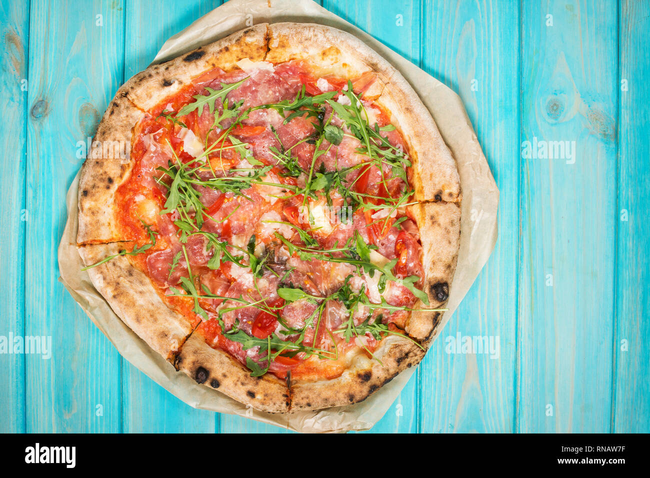 Pizza con prosciutto, rúcula y parmesano sobre azul de fondo de madera. Vista desde arriba. Comida italiana tradicional. Foto de stock