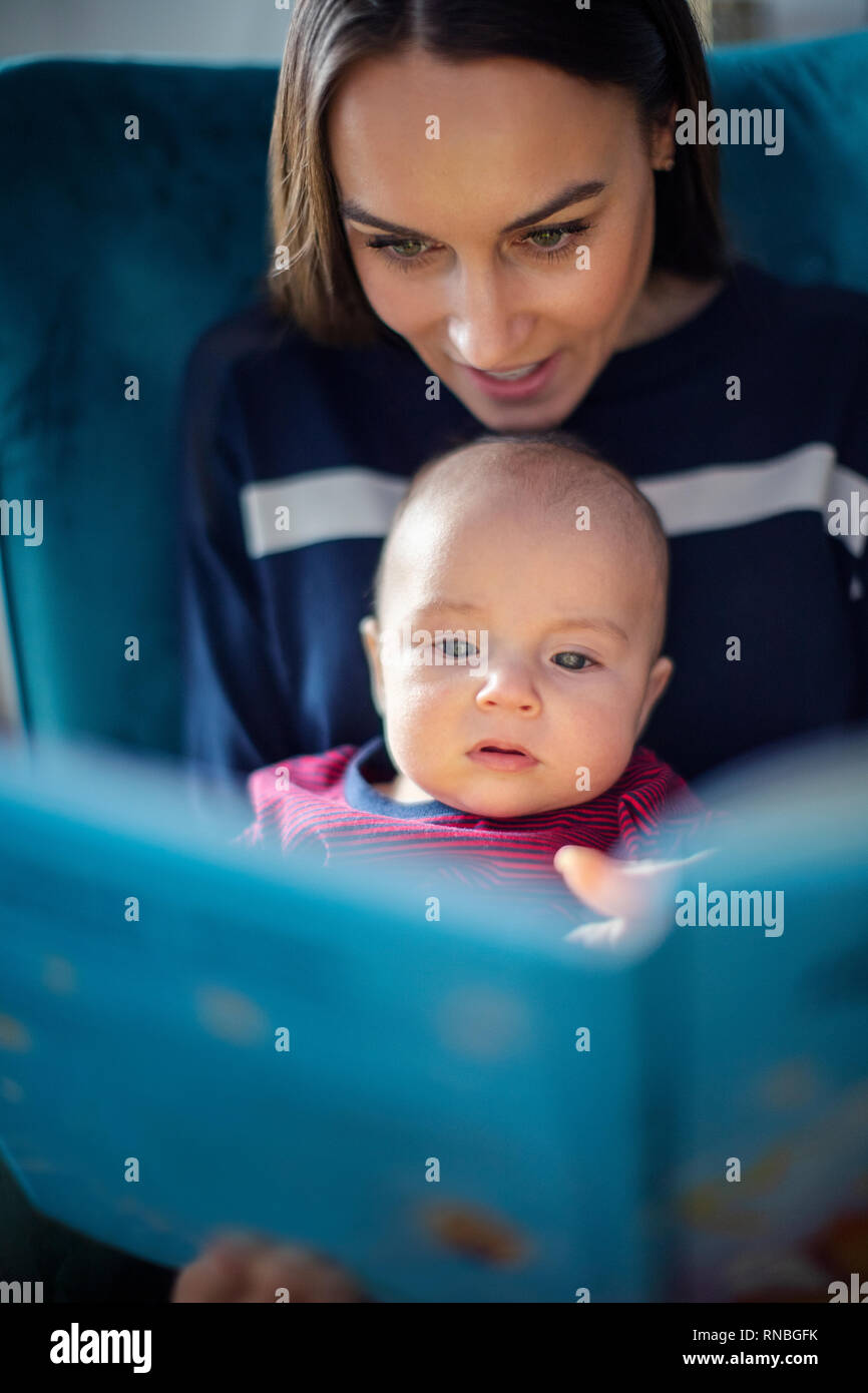 Hijo sentado en el regazo de las madres leer historia libro juntos Foto de stock