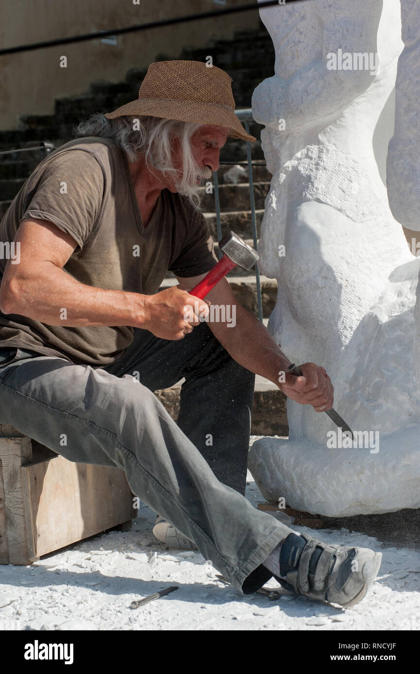 Escultor Senior trabajando en el exterior en su taller de escultura de mármol con un martillo y un cincel Foto de stock