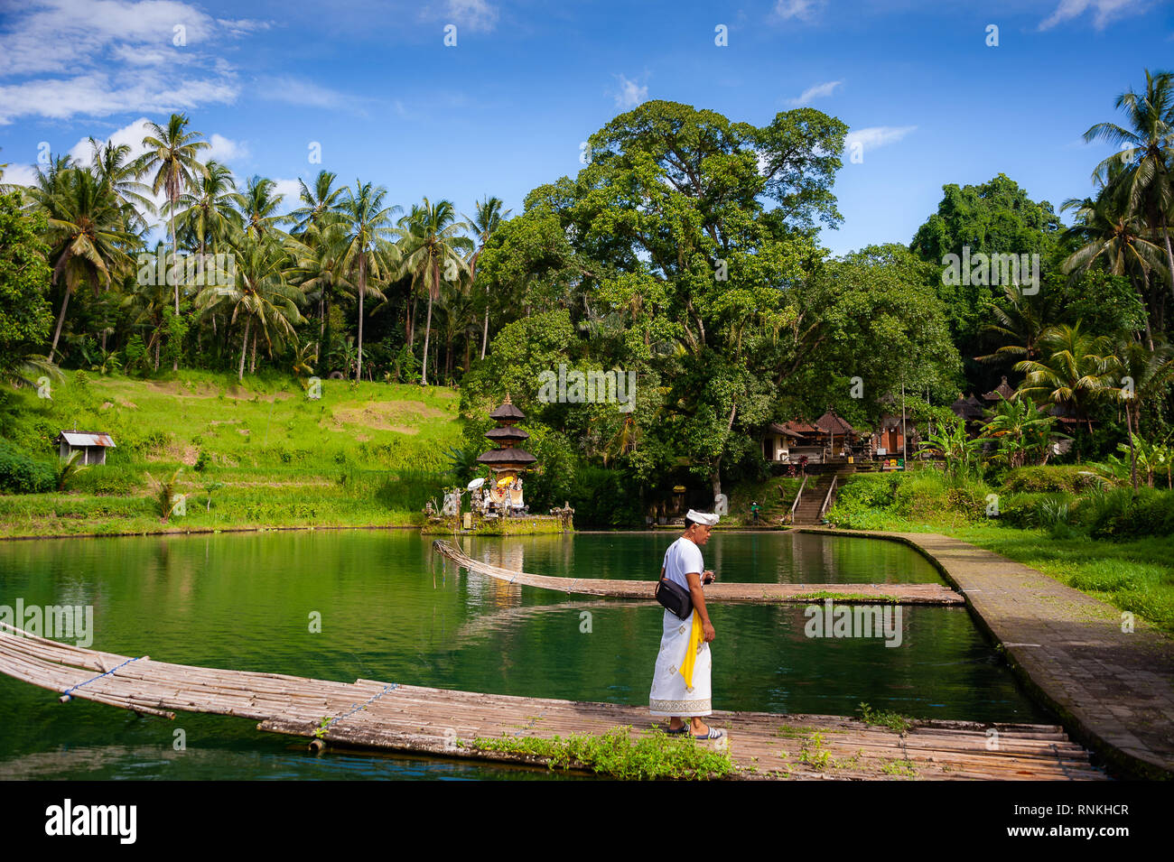 Hombre con traje tradicional balinesa visita Taman Tirta Mumba, templo del agua para celebrar una fiesta religiosa. Hermoso lago, naturaleza del paisaje Foto de stock