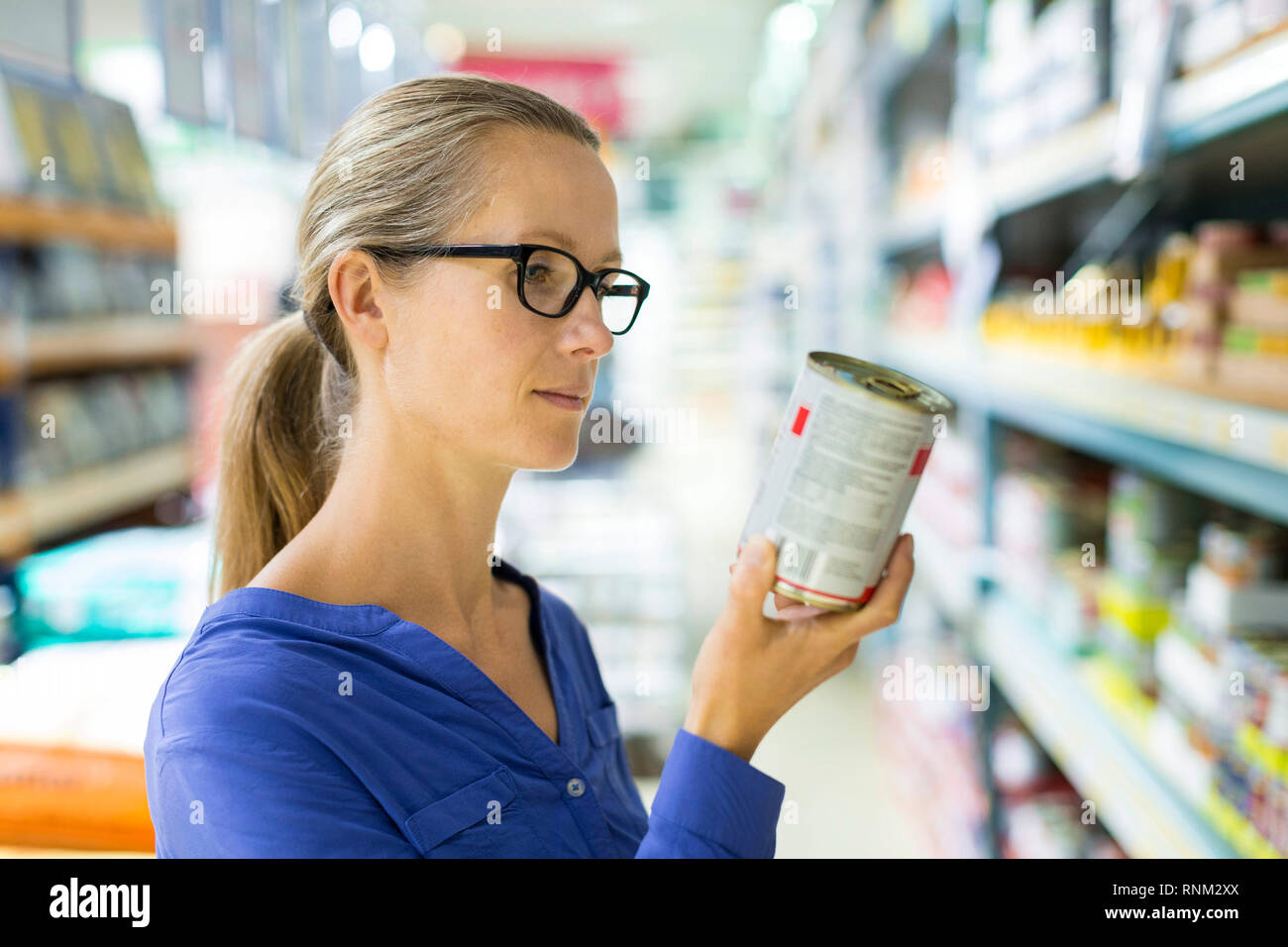 Mujer estudiando en la etiqueta de alimentos enlatados húmedos pueden delante de un estante en una tienda. Alemania. Foto de stock