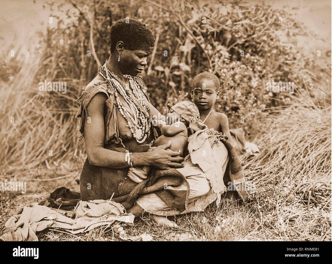 Mujer africana con dos pequeños asientos para niños en la hierba, 1916, Durban, Sudáfrica Foto de stock
