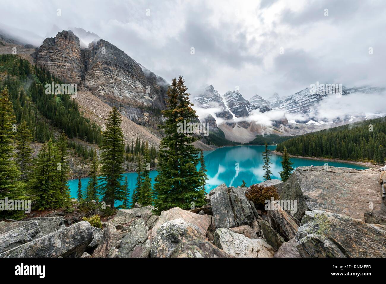 Las nubes colgando entre los picos de la montaña, la reflexión en turquesa del lago glacial, el Lago Moraine, el Valle de los Diez Picos, Montañas Rocosas, Banff unidas Foto de stock