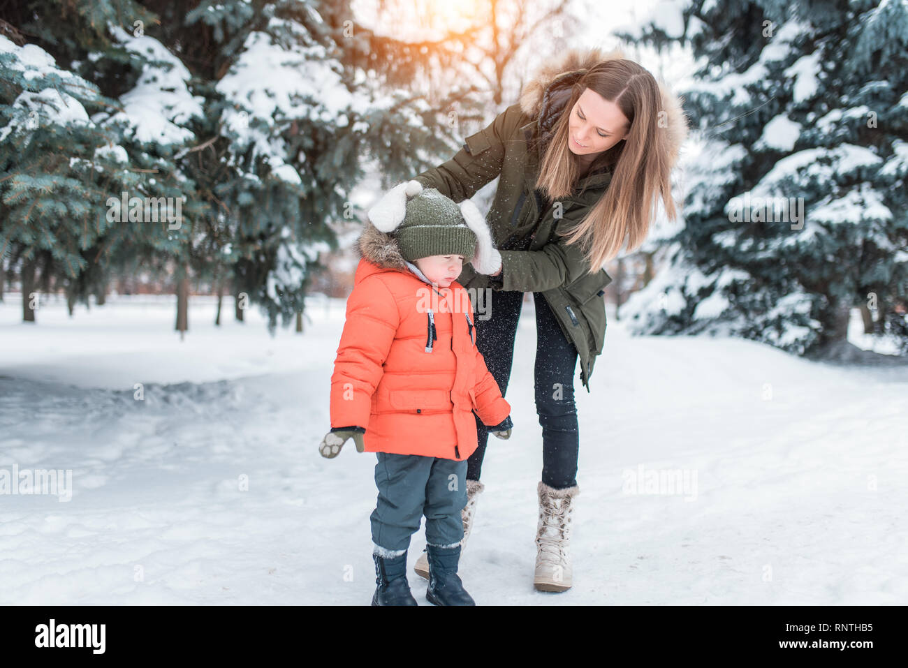 Mujer joven madre sacude la nieve sombrero del niño 3-5 años de edad, hijo  de ropa de invierno. En invierno, en el bosque en el complejo turístico  donde hay Fotografía de stock -