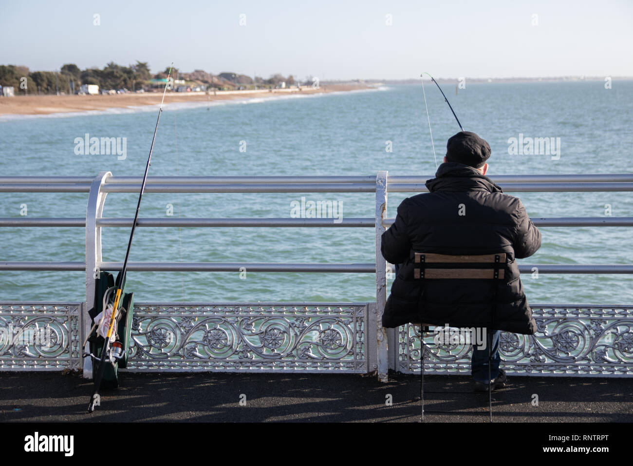 Hombre que pesca fuera de un inglés victoriano pier sentado en un taburete  con cañas de pescar la cuaresma contra las barandillas Fotografía de stock  - Alamy