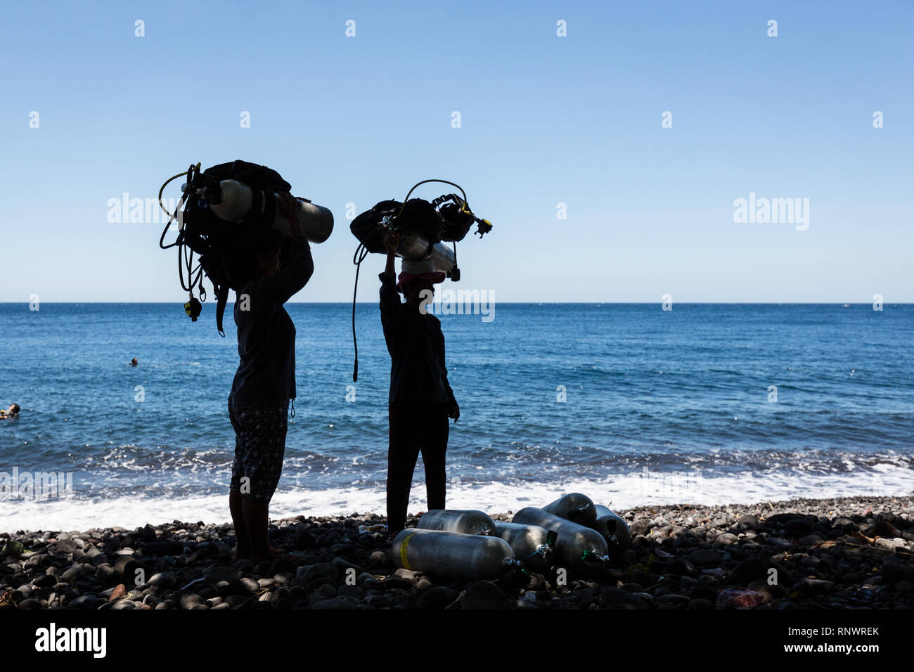 Dos mujeres portan pesadas scuba diving gear sobre sus cabezas, un sitio común en Tulemban, Bali, Indonesia. Foto de stock