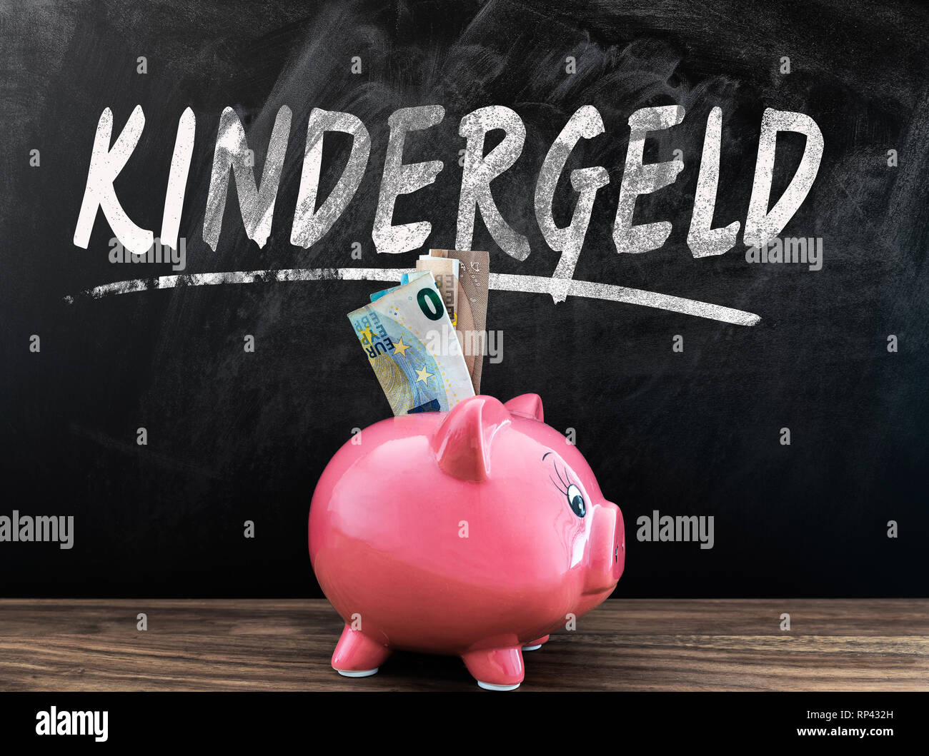 Palabra KINDERGELD, Alemán para el subsidio, en pizarra con hucha y efectivo en frente a la mesa de madera Foto de stock