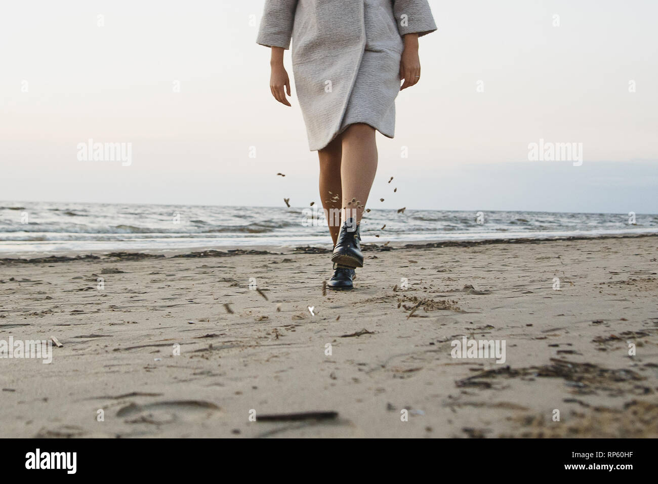 Mujer despreocupada en botas de cuero negro patada en la playa de arena. Volando arena mojada. Concepto El calzado de protección, resistencia al agua y al polvo. Foto de stock