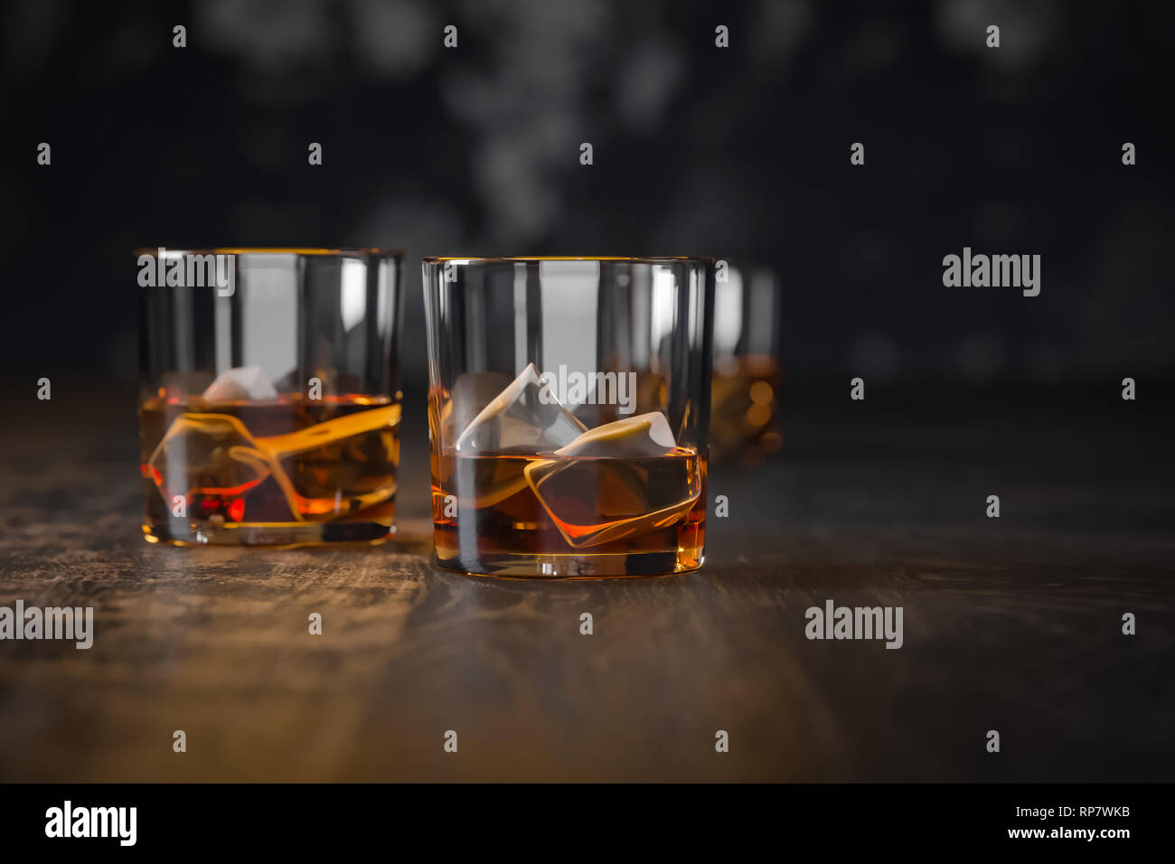 Tres vasos de whisky con hielo, stand en una oscura mesa de madera antigua y un fondo negro Foto de stock