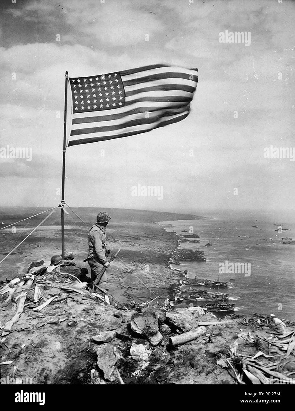 Desde la cima del monte Suribachi, el Stars & Stripes de onda en triunfo sobre Iwo Jima después de marines estadounidenses habían luchado su manera centímetro a centímetro hasta sus escarpadas laderas de lava incrustada Foto de stock