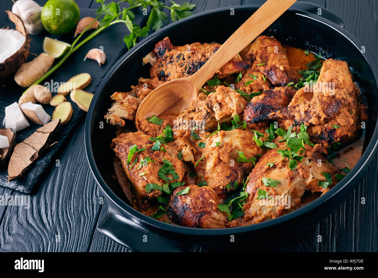 Kuku Paka, Keniana chargrilled pollo estofado en salsa de coco picante cremoso servido en cazuela de barro sobre una mesa de madera. Los ingredientes sobre una piedra cu Foto de stock