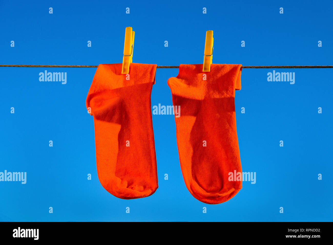 Dos nuevos, limpios, lavados, naranja calcetines colgando en una cuerda con amarillo clothespins. fondo de cielo azul Foto de stock