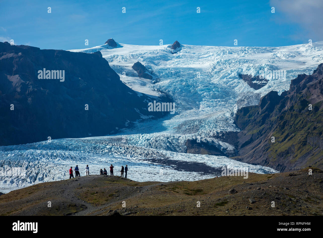 Las personas empequeñecidas por debajo de la caída de hielo glaciar Kviarjokulll. Casquete glaciar Vatnajokull, Sudhurland, sudeste de Islandia. Foto de stock