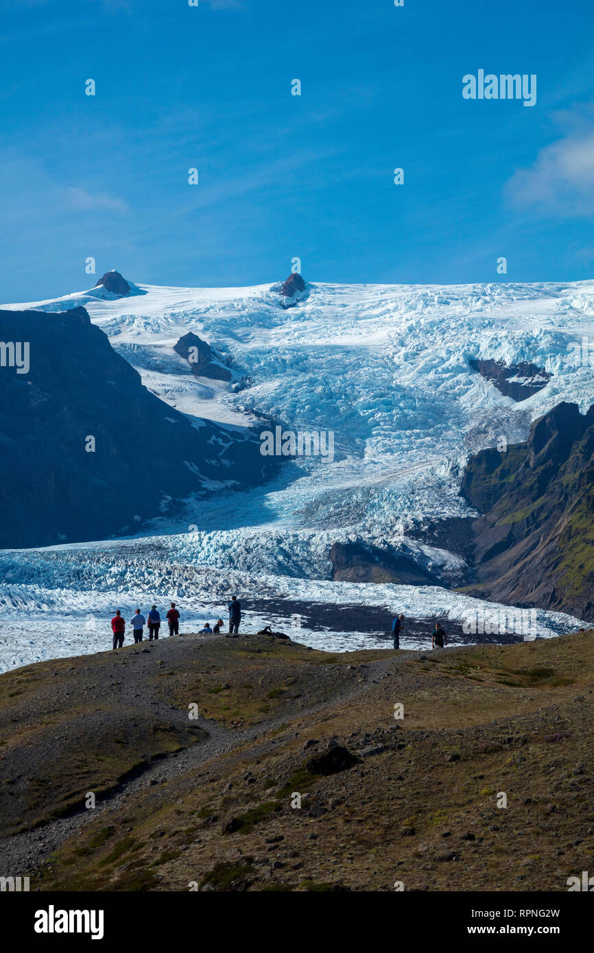 Las personas empequeñecidas por debajo de la caída de hielo glaciar Kviarjokulll. Casquete glaciar Vatnajokull, Sudhurland, sudeste de Islandia. Foto de stock