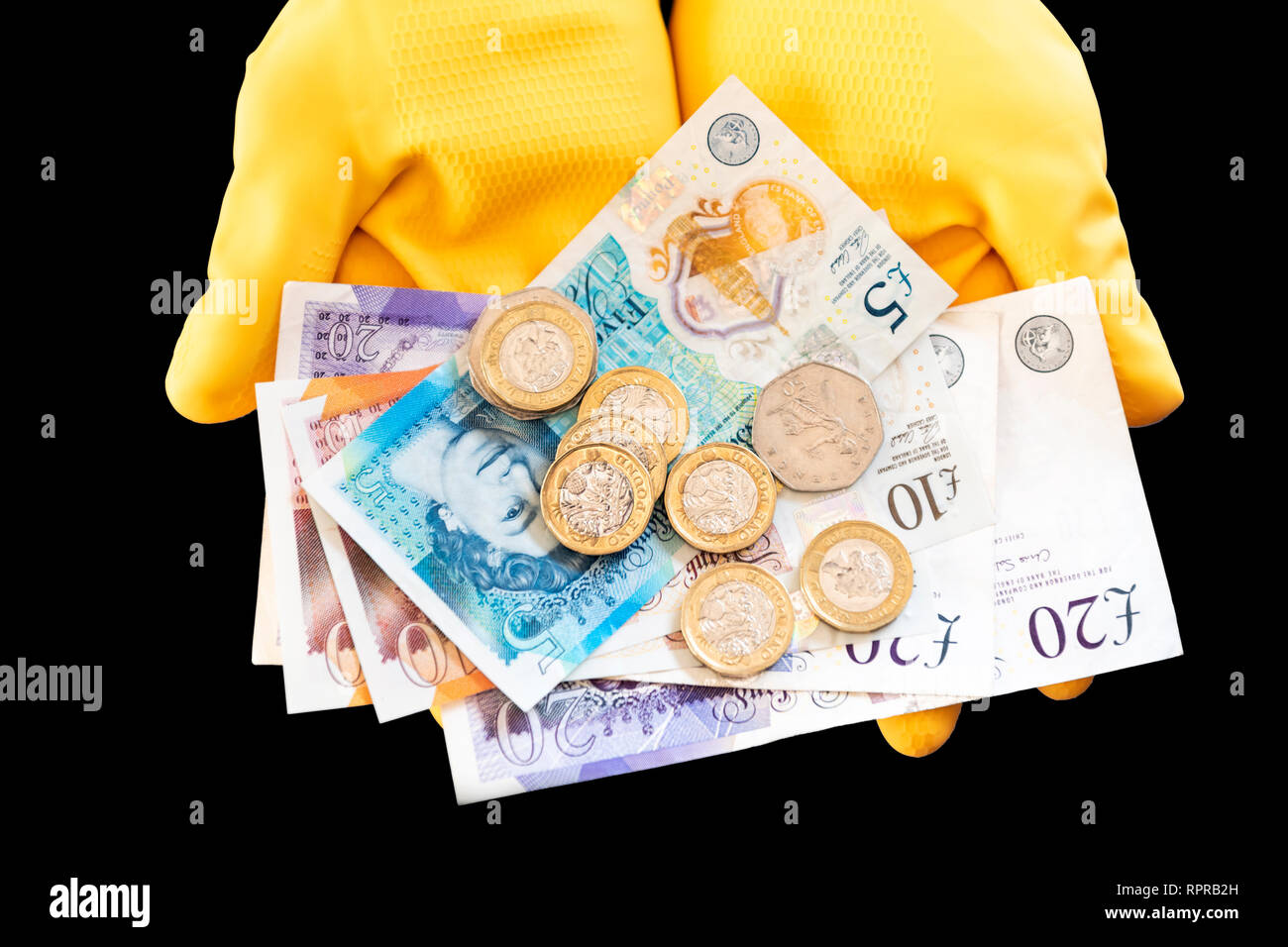Un par de manos usando guantes de goma amarilla celebración pound notas y monedas. Concepto de dinero en efectivo, la economía sumergida o de baja remuneración. Foto de stock