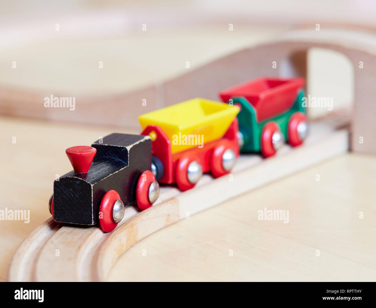 Tren de juguete de madera en miniatura, corriendo en las pistas. El motor negro tirando de coches de colores en el suelo. Juguetes educativos para niños en edad preescolar y amables Fotografía