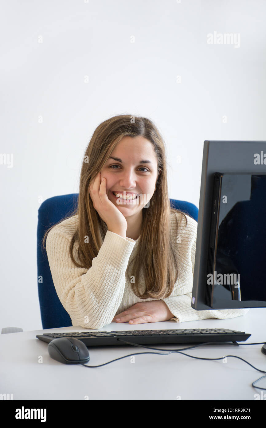 joven secretario sonriente en el trabajo en una oficina blanca frente a la computadora. Concepto de servicio al cliente agradable y alegre. Foto de stock
