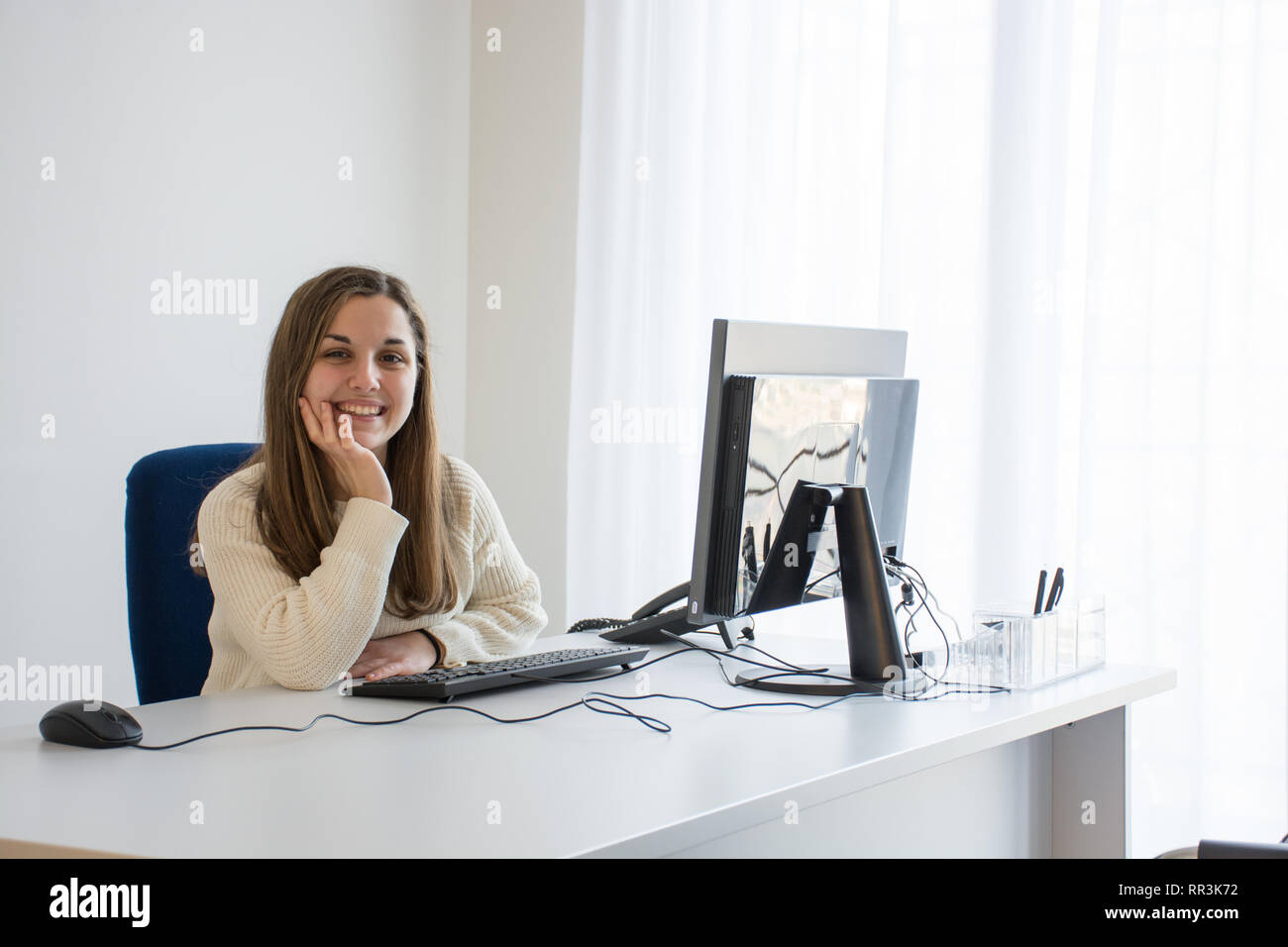 joven secretario sonriente en el trabajo en una oficina blanca frente a la computadora. Concepto de servicio al cliente agradable y alegre. Foto de stock
