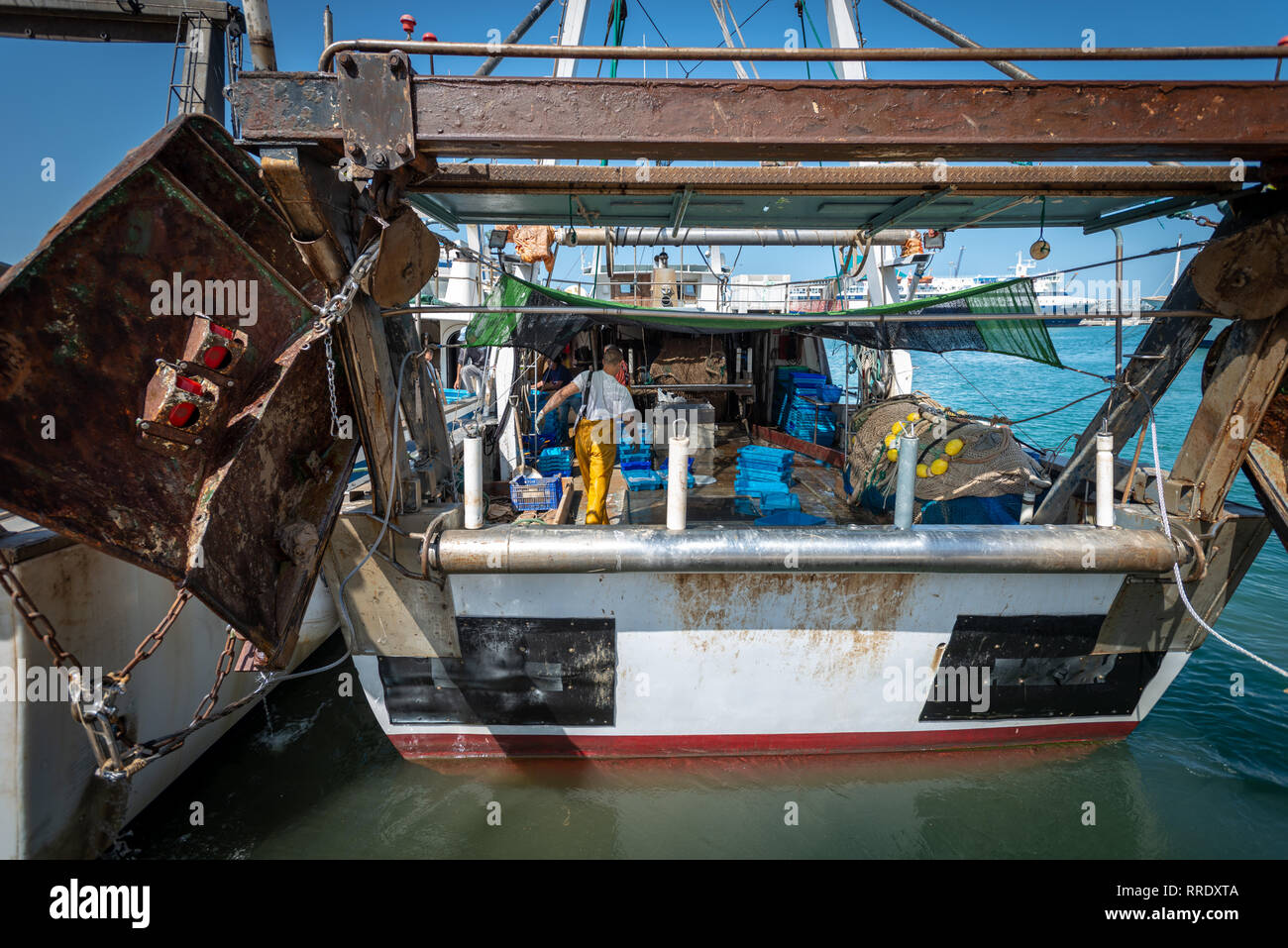 Un pescador vistiendo monos amarillos tidies equipos sobre la cubierta de un arrastrero de pesca en el puerto de Denia, España. Foto de stock