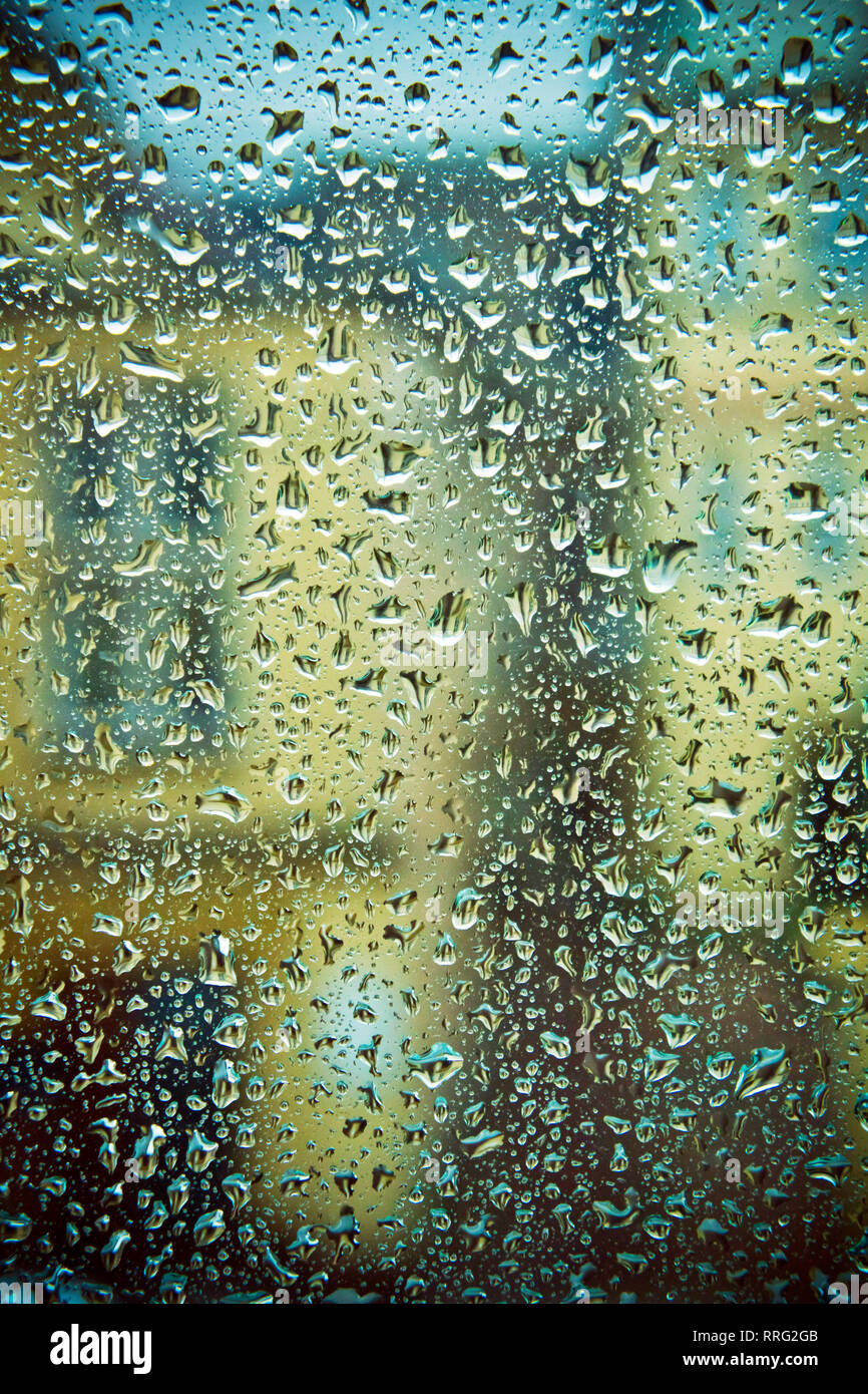 Cristal de la ventana cubierta con gotas de lluvia y casas detrás Foto de stock