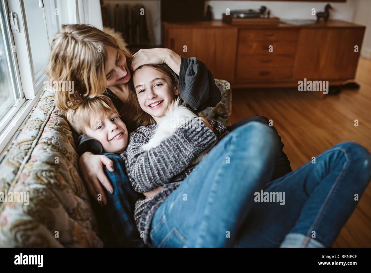 Retrato madre afectuosa y niños con cuy en el sofá de la sala Foto de stock