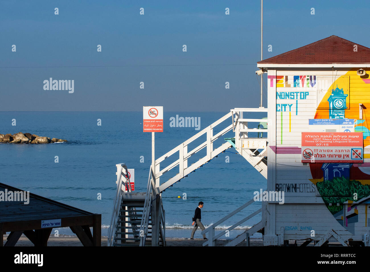 Hombre caminando por la playa al amanecer Tayelet, por un socorrista stand convertido temporalmente en un lujoso hotel suite forma parte de un proyecto de turismo promocional Foto de stock