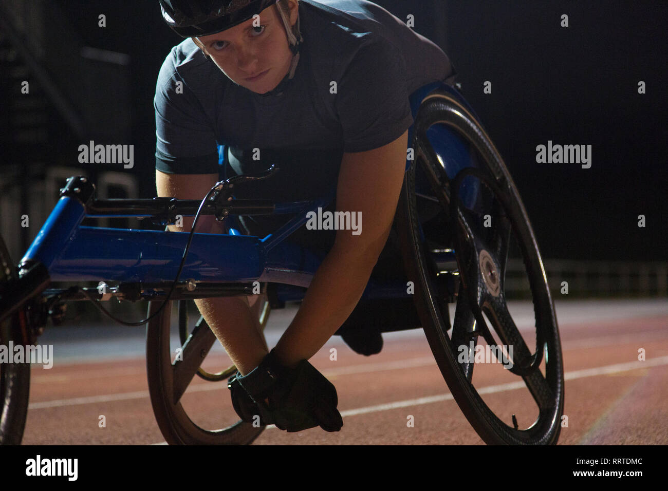 Retrato determinada joven atleta parapléjico entrenamiento para carrera de silla de ruedas en la pista de deporte en la noche Foto de stock