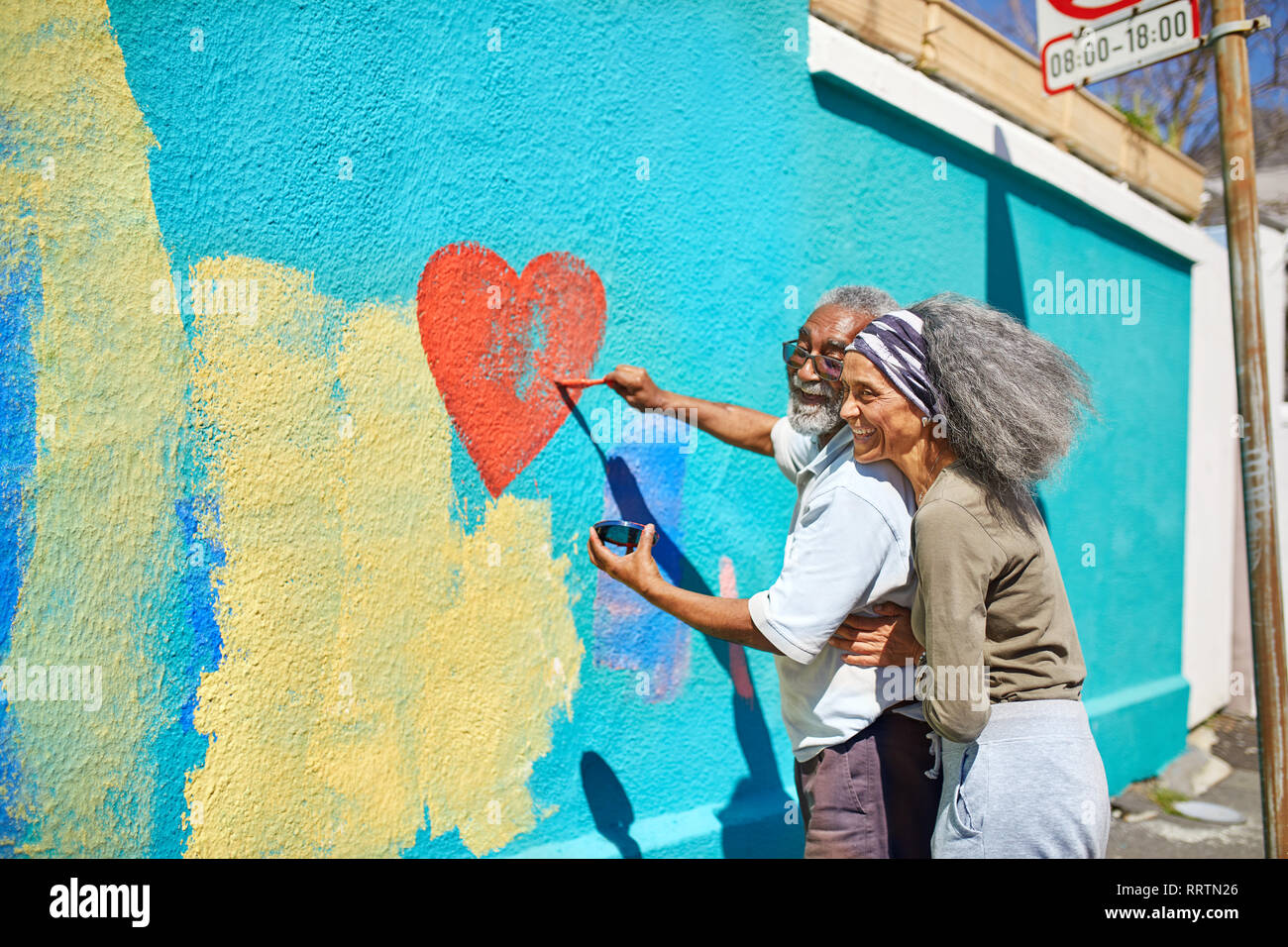 Feliz pareja senior pintura mural en forma de corazón en la pared soleada Foto de stock