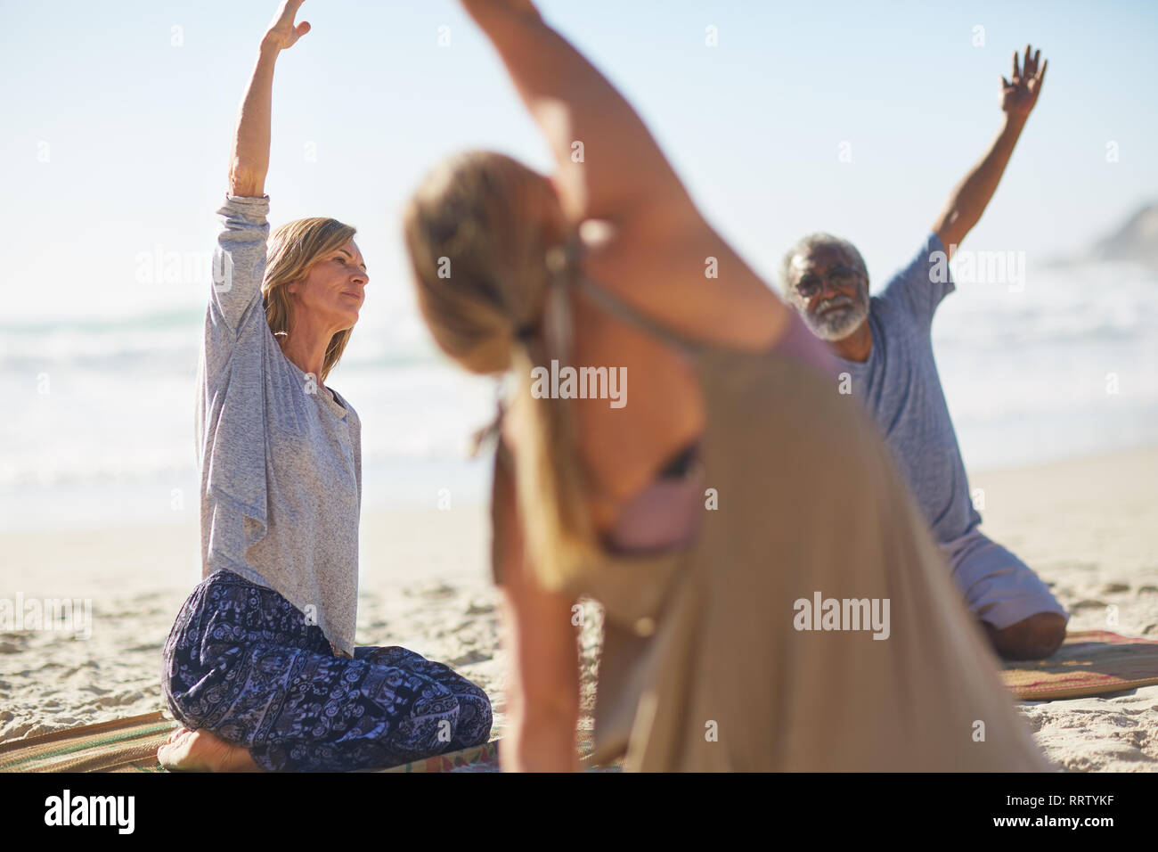Grupo stretching en sunny beach durante yoga retreat Foto de stock
