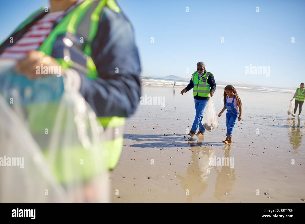 Abuelo y nieta voluntarios, la limpieza de la basura en la soleada playa de arena húmeda Foto de stock