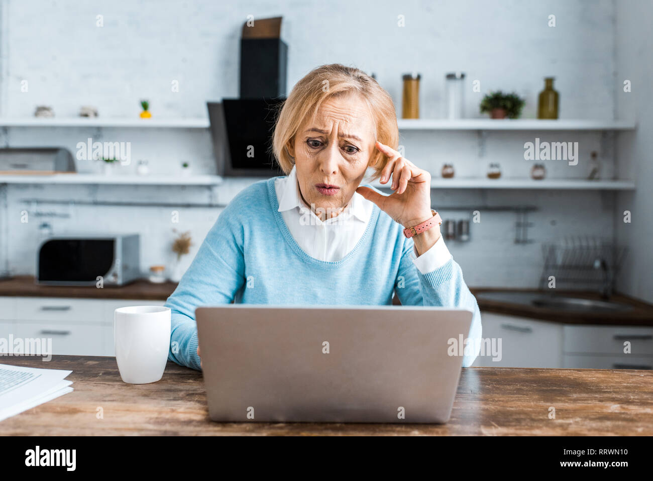 Conmocionado mujer senior de tocar la cara, con ordenador portátil y tener video  chat en la cocina Fotografía de stock - Alamy