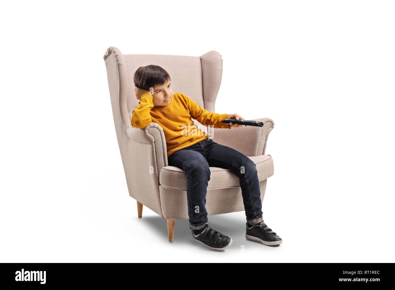 Disparo de longitud completa de un aburrido chico sentado en un sillón y manteniendo un control remoto aislado sobre fondo blanco. Foto de stock