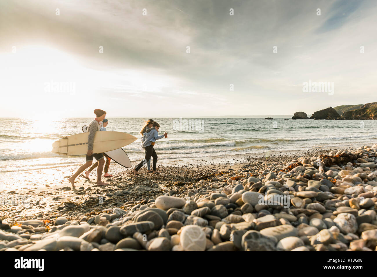 Feliz amigos con tablas de surf caminar sobre la playa de grava Foto de stock
