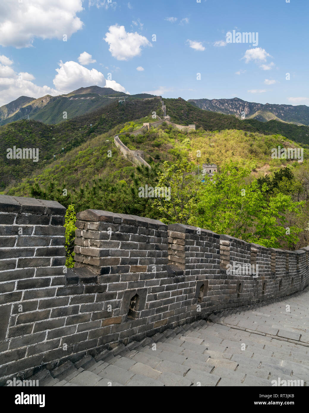 Los empinados escalones de piedra de la Gran Muralla de China en Mutianyu en primer plano. Varias torres de vigilancia puede ser visto como la pared sube a las montañas. Foto de stock