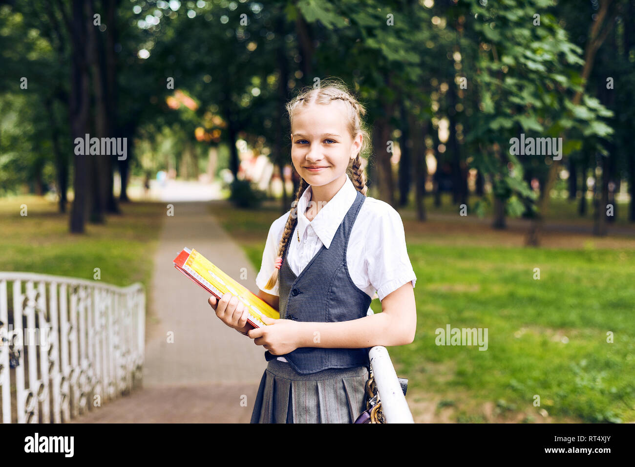 Retrato de una estudiante adolescente en uniforme con una mochila, en un parque cerca de un gran árbol. colegiala leyendo un libro Foto de stock
