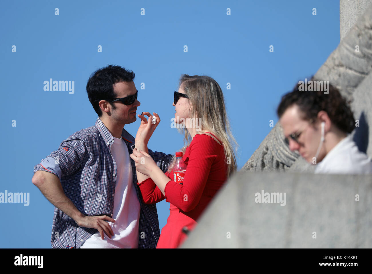 Clima caluroso de febrero de 2019 los amantes y hacer reír, bromear y aplicar lip salve en la columna de Nelson en Trafalgar Square con el National Gallery en la espalda Foto de stock