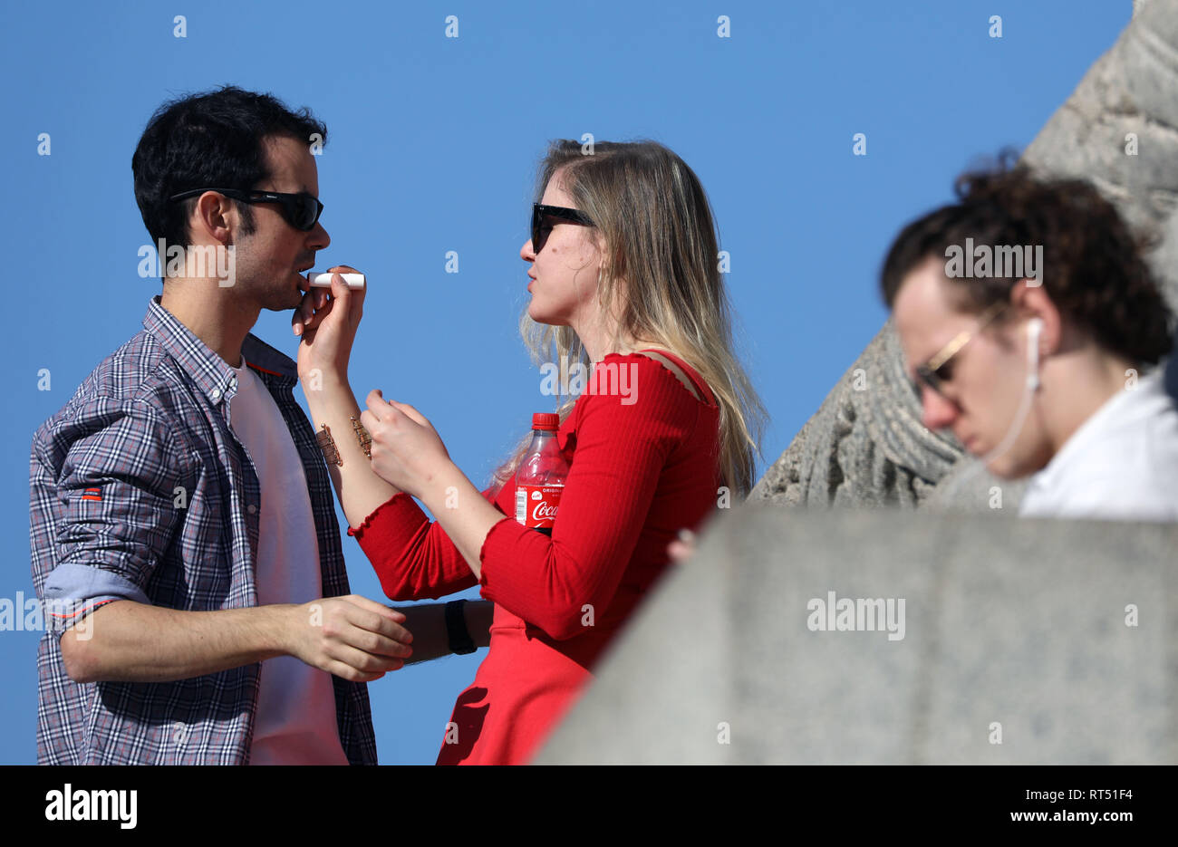 Clima caluroso de febrero de 2019 los amantes y hacer reír, bromear y aplicar lip salve en la columna de Nelson en Trafalgar Square con el National Gallery en la espalda Foto de stock