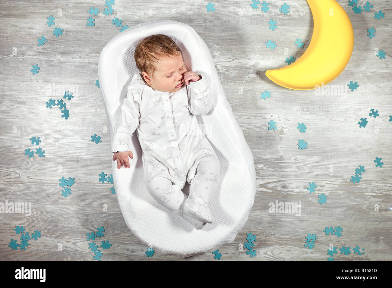 Bebé recién nacido duerme tranquilamente en un colchón ortopédico especial  bebé cocoon, piso de madera y luna de juguete rompecabezas alrededor. La  calma y el sueño sano en nueva Fotografía de stock -