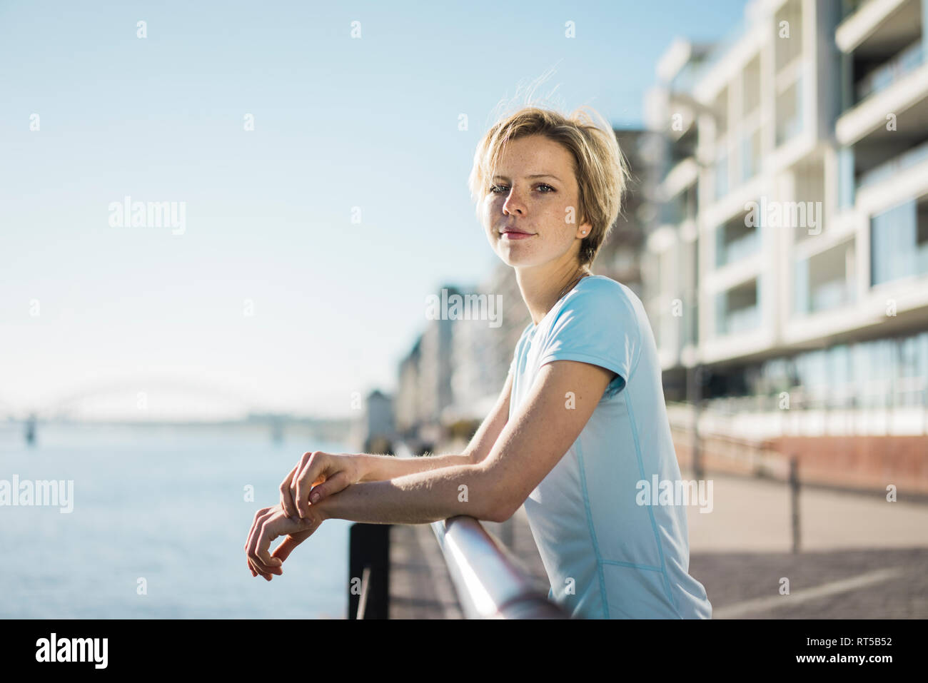 Mujer joven de pie en la orilla del río, disfrutando del sol Foto de stock